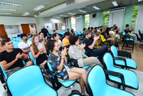 Um grupo de alunos e alunas estrangeiros sentadas em um auditório da Unicamp batendo palmas